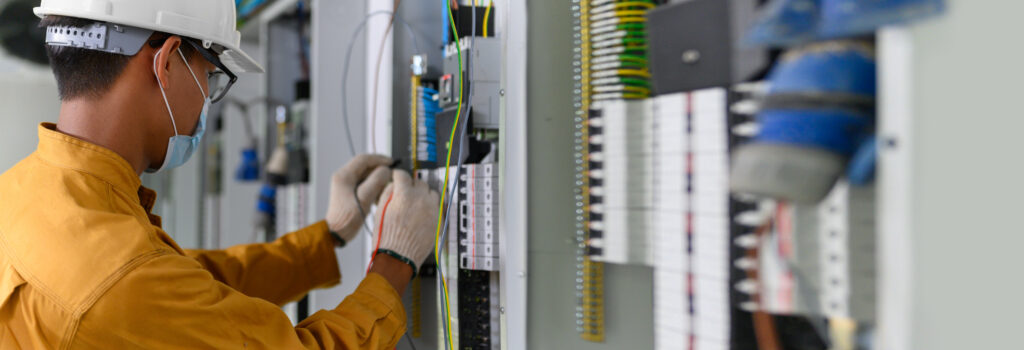 Electrician engineer using digital multimeter test current electric in control panel ​for testing electrical installations and wiring work in power control room on new building.