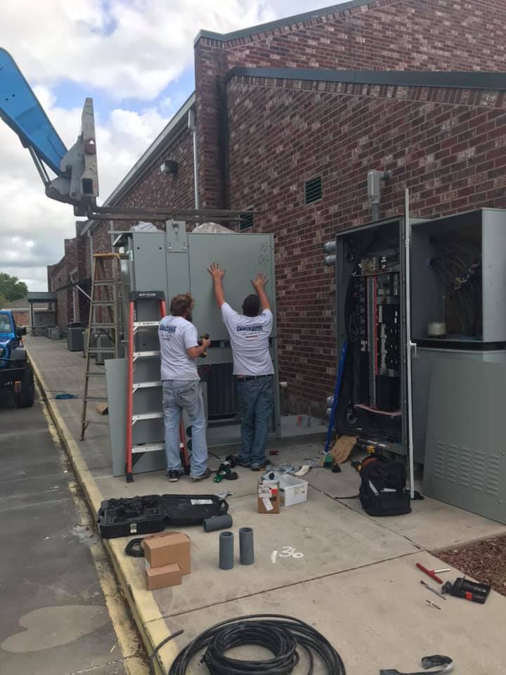 Two electricians inspecting an open electrical panel
